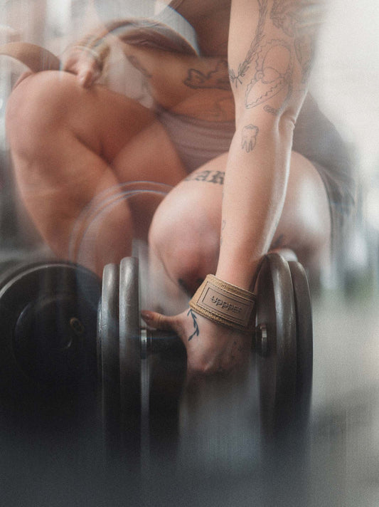 woman gripping dumbbell wearing uppper lifting straps